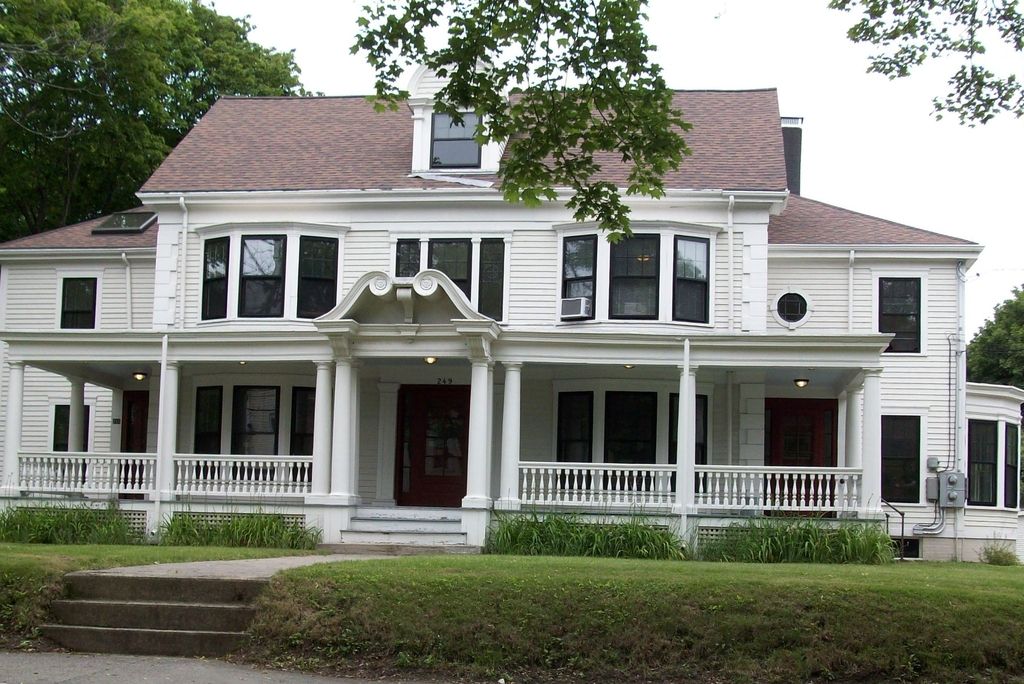 A white two-storey house with a long front porch and balustrade