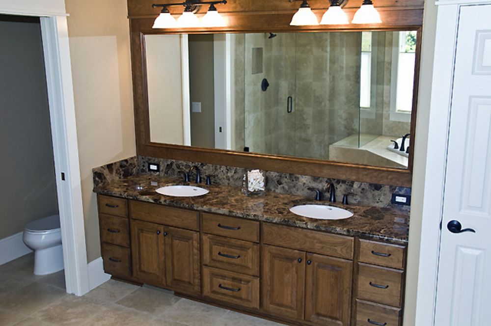 A large bathroom with a granite double vanity, wood cabinets and a wide mirror