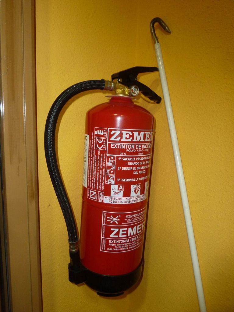 A red fire extinguisher mounted on a warm yellow wall