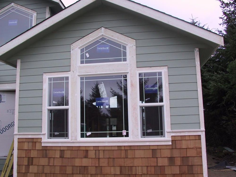A bright new bay window set into a sage green wall with cedar shingles